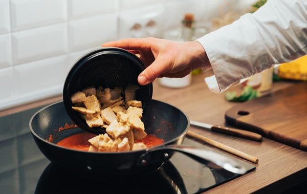 Pollo versato nella salsa in padella per finire la preparazione del Chicken Tikka Masala